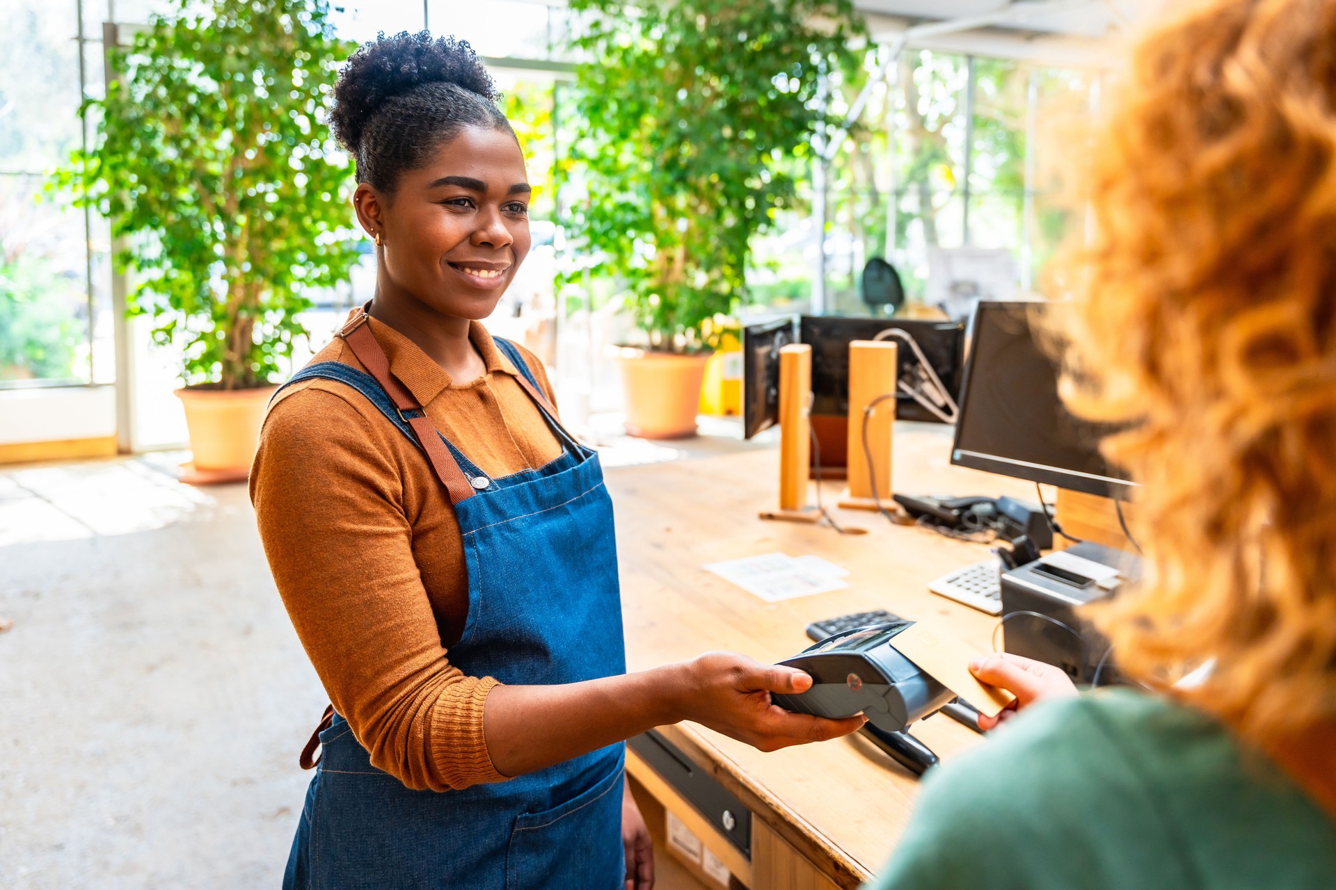 Smiling cashier accepting contactless payment from customer in plant store