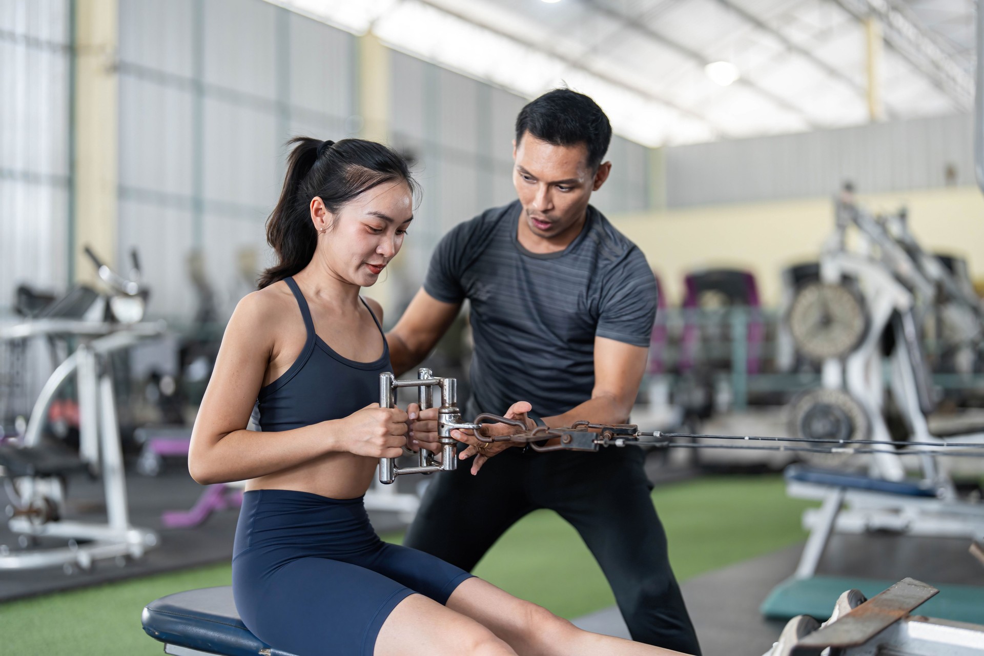 Personal Training and Strength Development. A trainer assisting a woman with cable exercises in a gym.