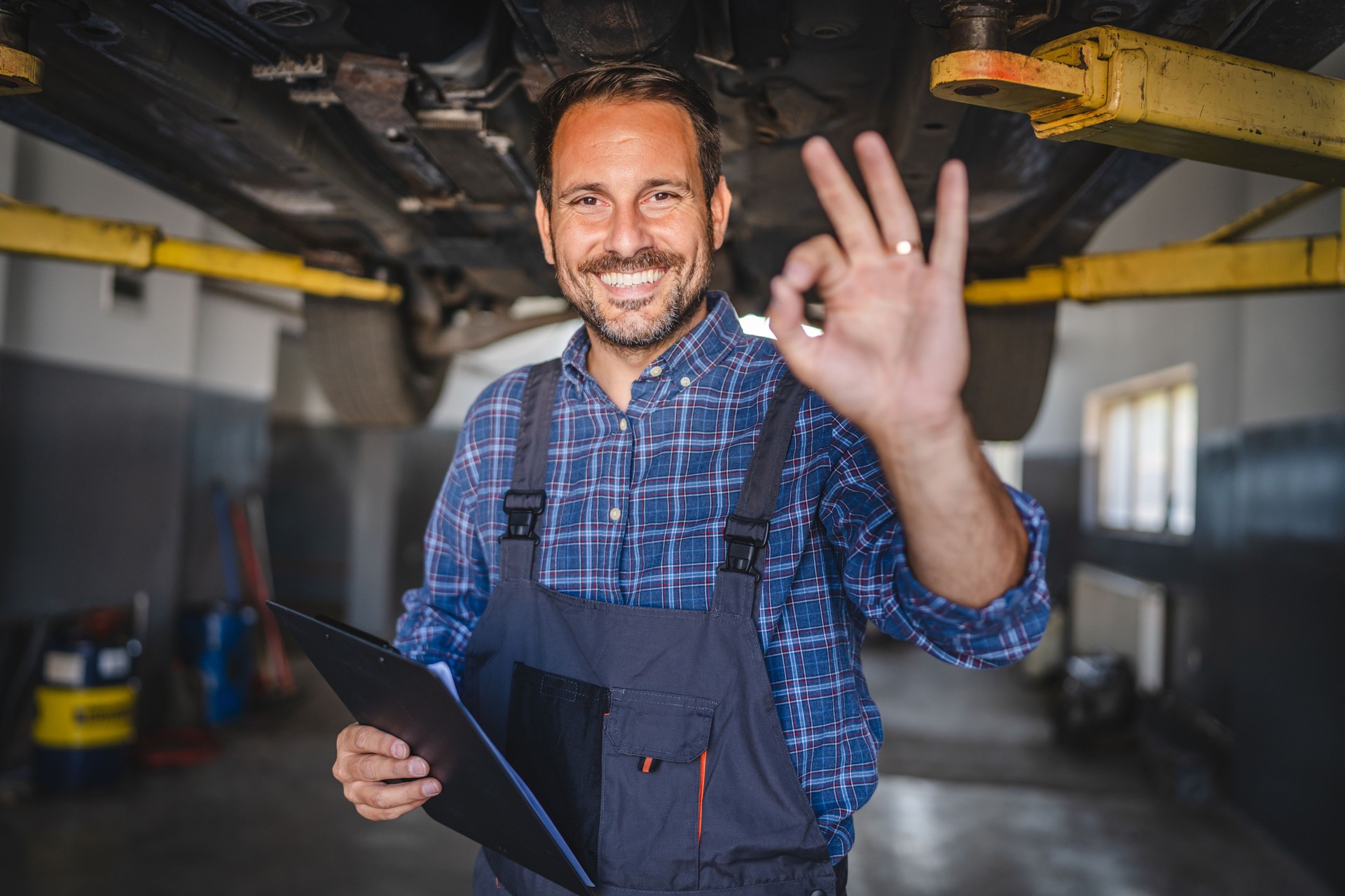 Car mechanic making gesture under the car with friendly smile