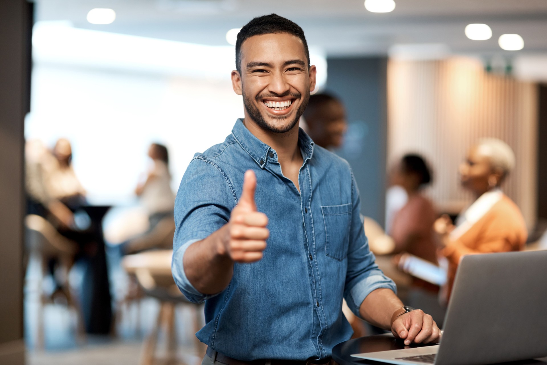 Shot of a young businessman showing thumbs up while using a laptop at a conference